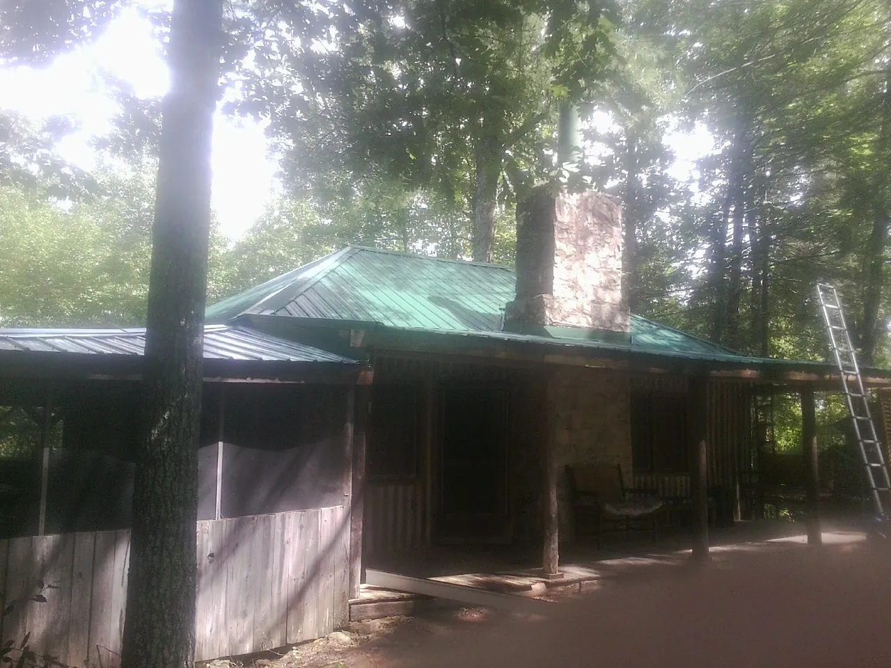 Green metal roof and stone chimney above a log cabin porch in Northfield