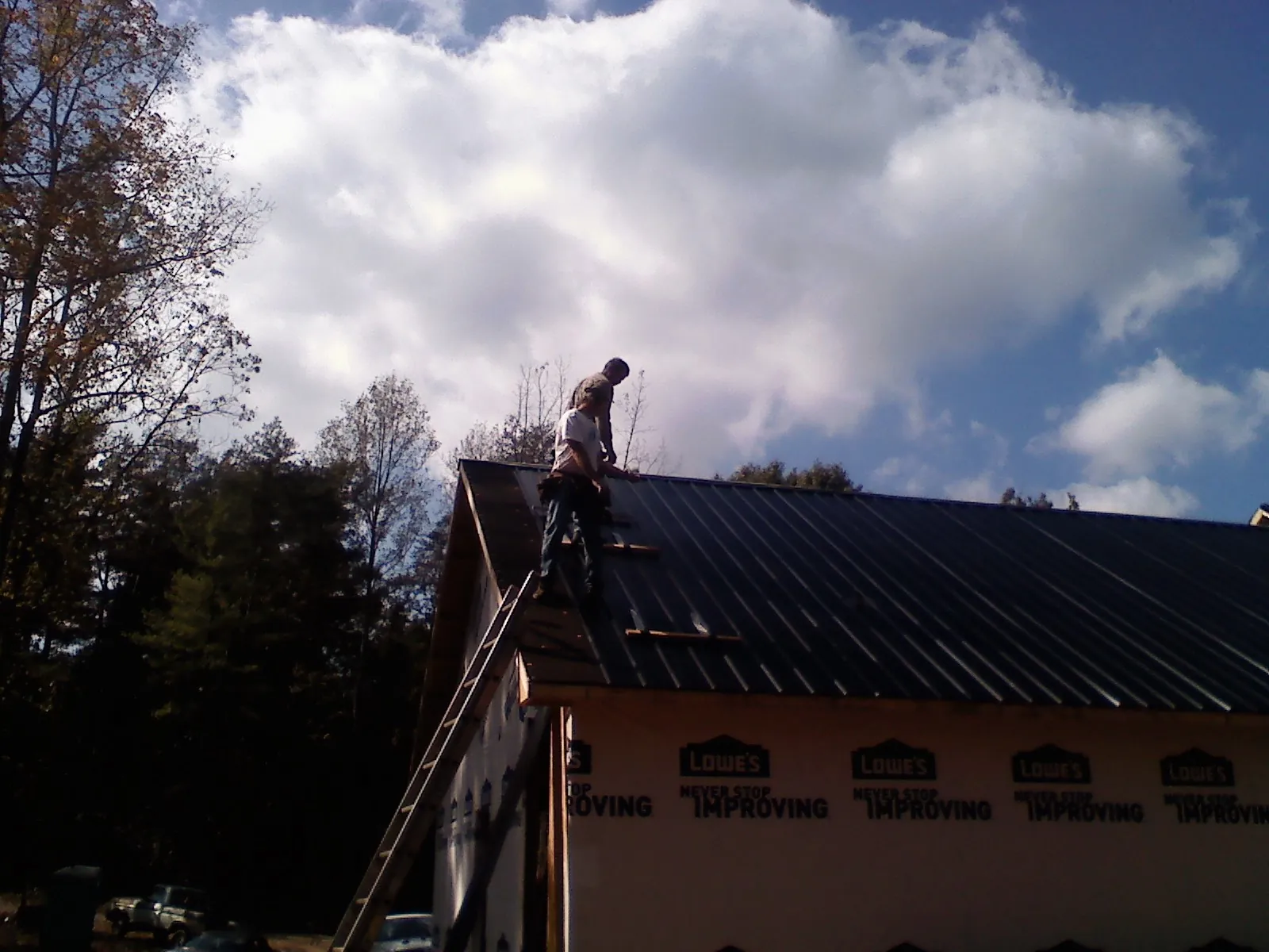 Roofer fastening dark metal panels high against a cloudy sky, from a Roof Inspection job in Northfield